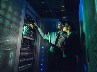 Two engineers examining server equipment in a dimly lit data center.  
