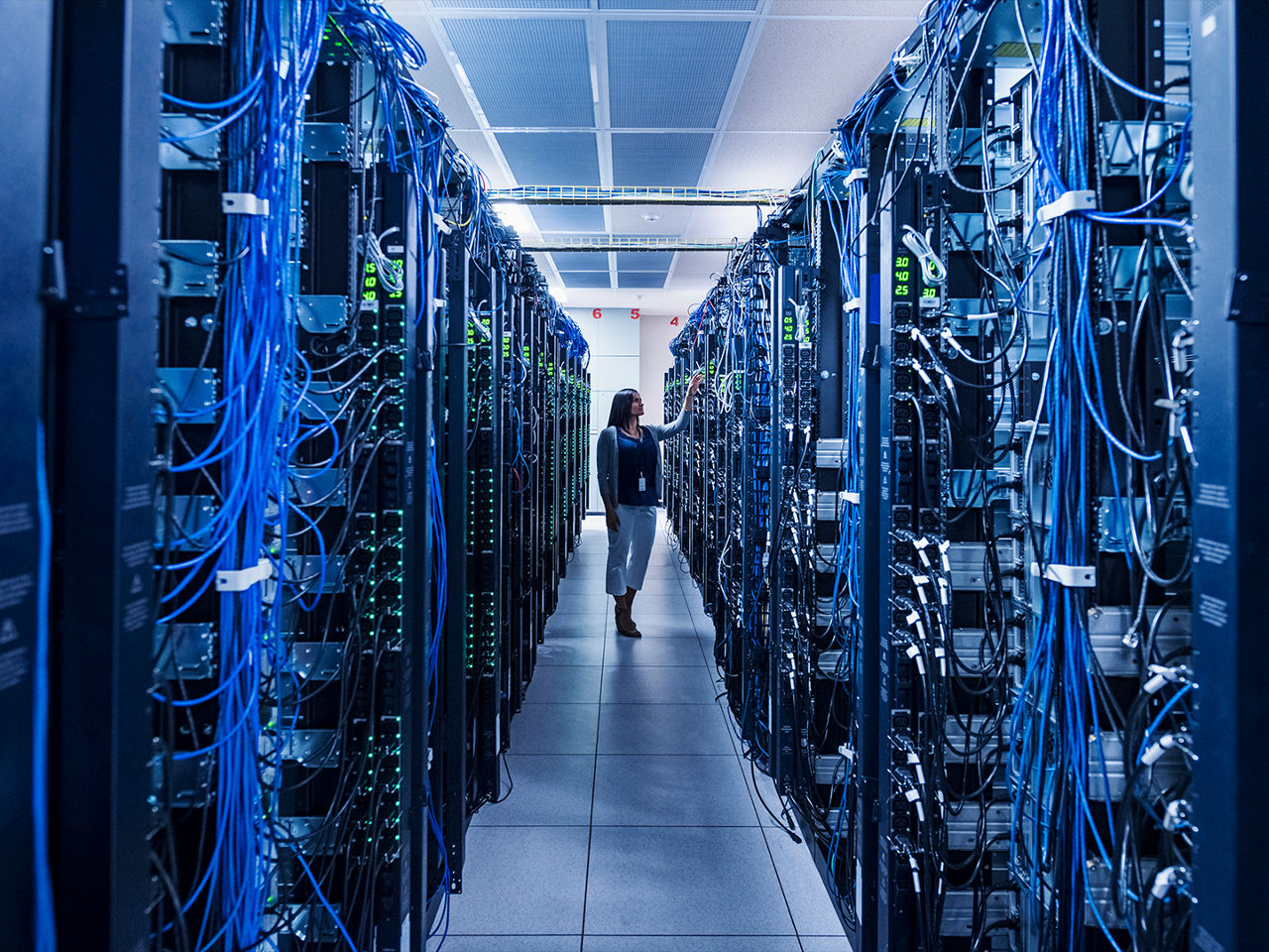 Person standing in a data center room filled with rows of server racks. 