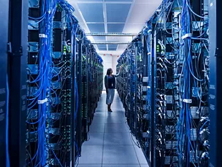 Person standing in a data center room filled with rows of server racks. 