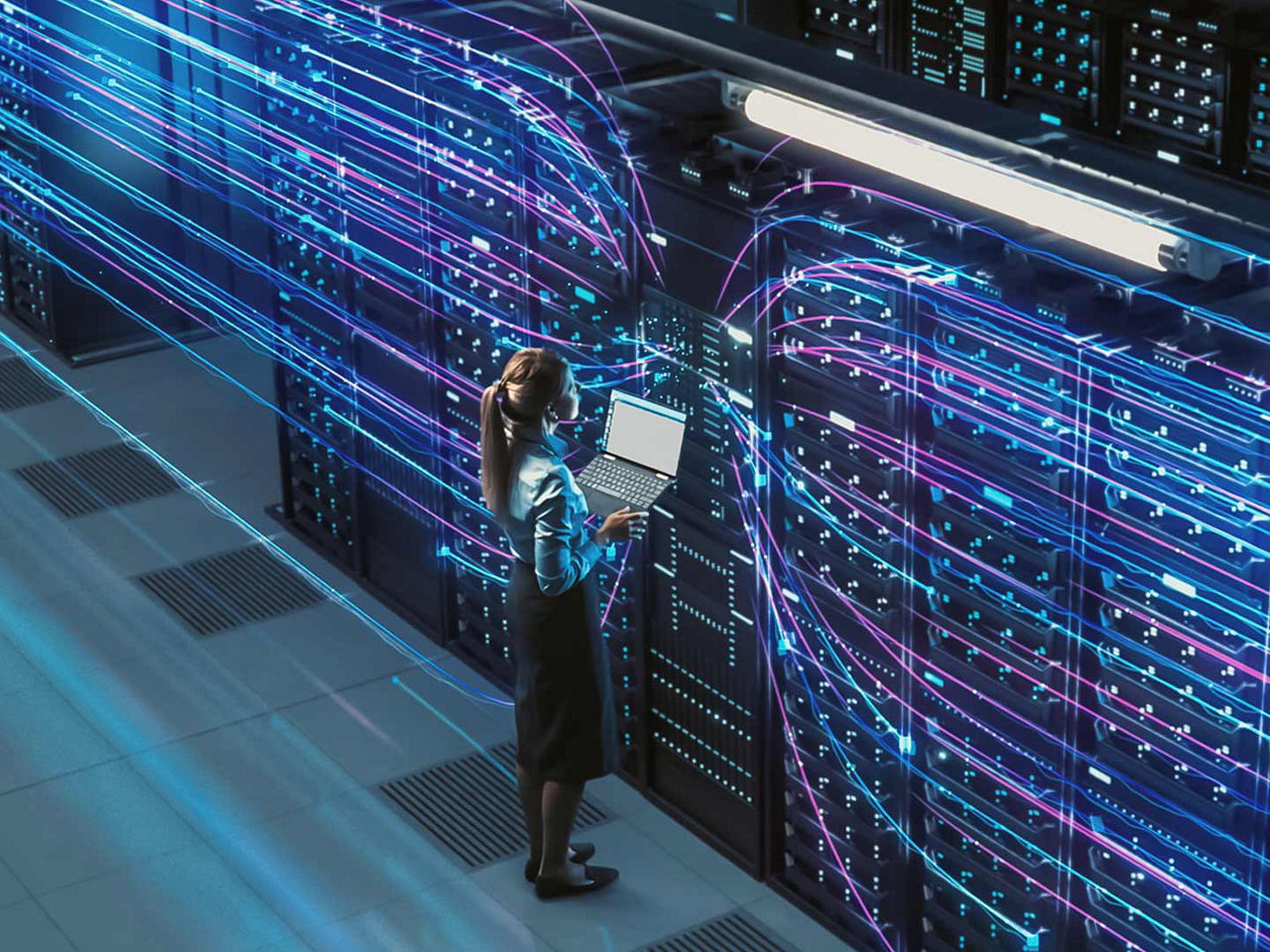 Woman standing inside a data center holding a laptop. 