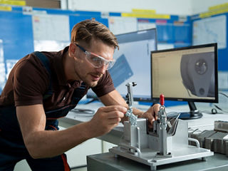 Engineer adjusts a component in a test fixture with a CAD model displayed on a nearby computer screen.