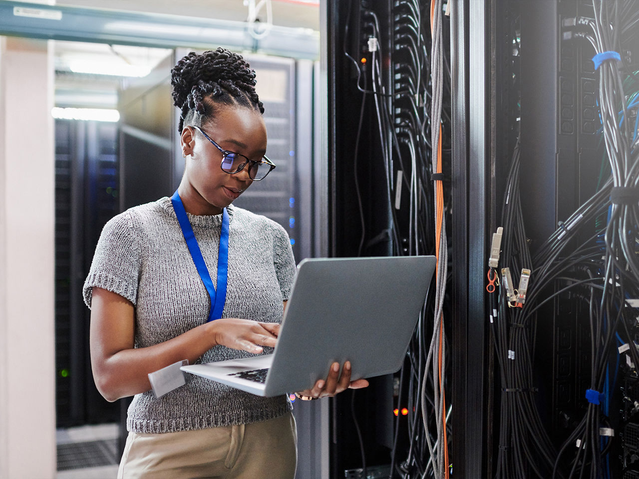 A young woman using a laptop in a data center server room. 