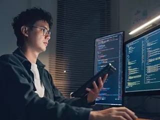 Developer examining code on two computer screens and a tablet.