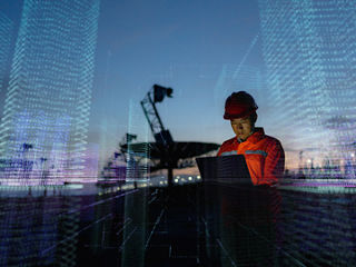 Engineer in safety gear using a laptop at a defense site, overlaid with digital data graphics representing smart technology and connectivity