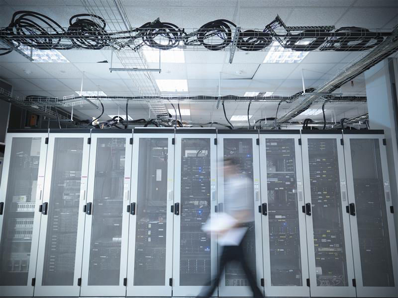 A motion-blurred technician walks past server racks in a high-performance data center.
