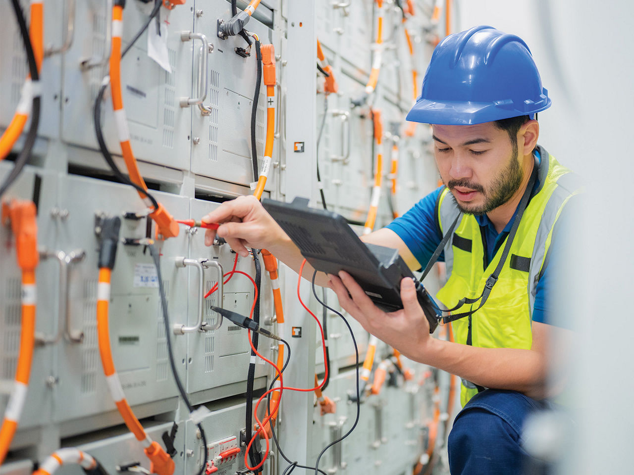 A male electrician working on a switchboard with an electrical connector cable. 