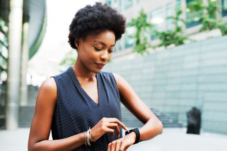 A woman uses a smartwatch outdoors in a modern city setting. 