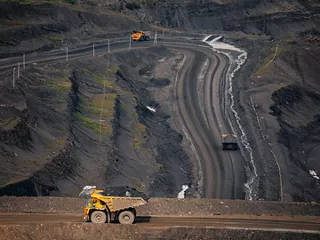A haul truck drives along a dirt road in a rugged open-pit mining environment.