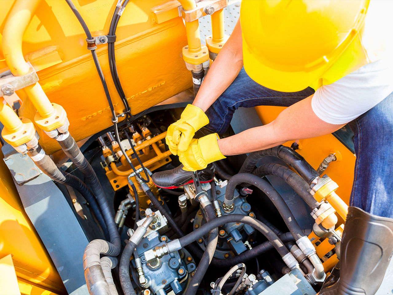 Mechanic performing field maintenance in a tight space within a construction vehicle.