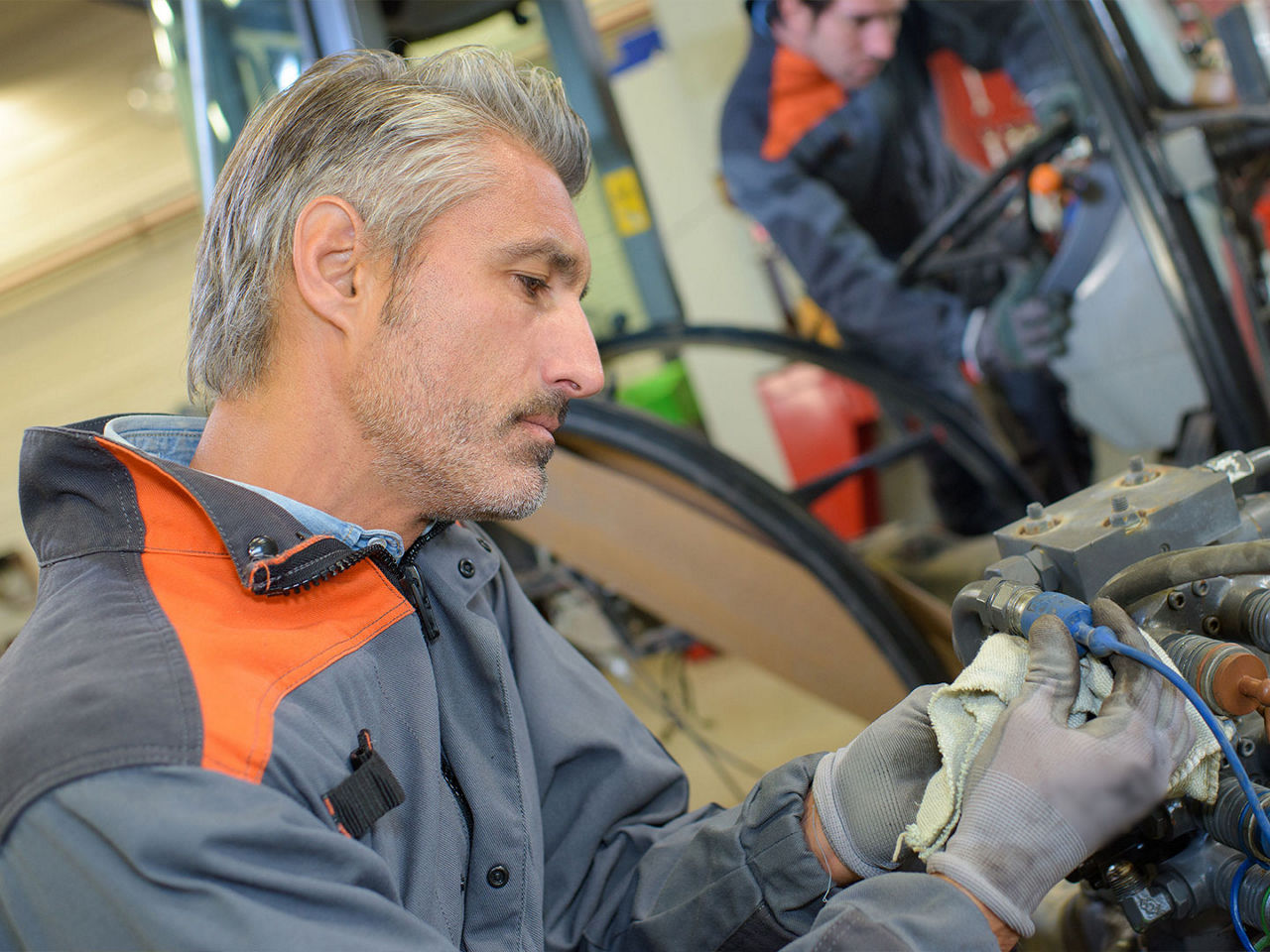 Mechanic manually connecting wires in a tractor engine.