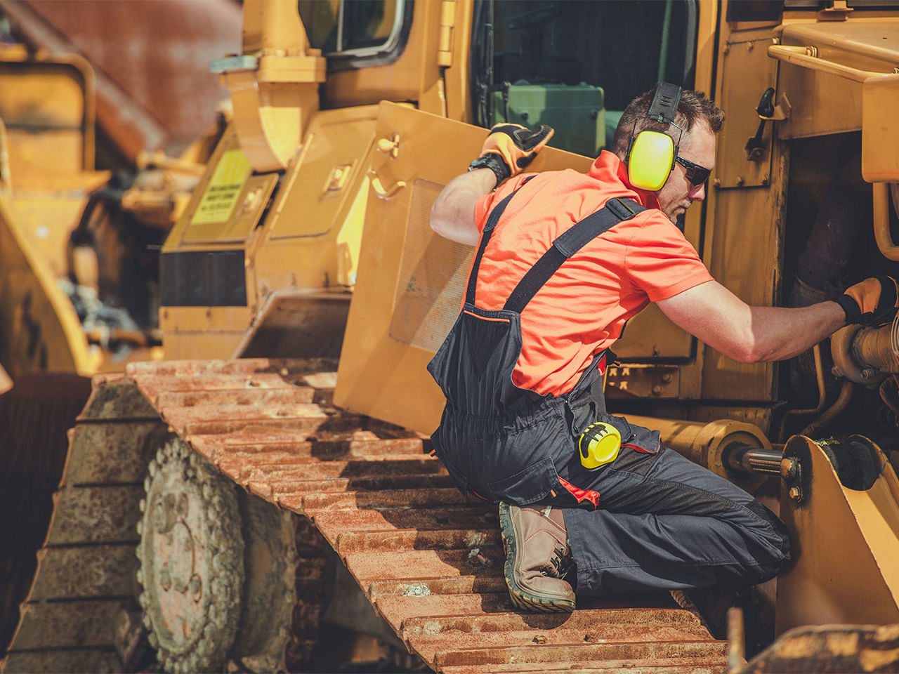 Technician performing maintenance on components behind a heavy equipment access panel.