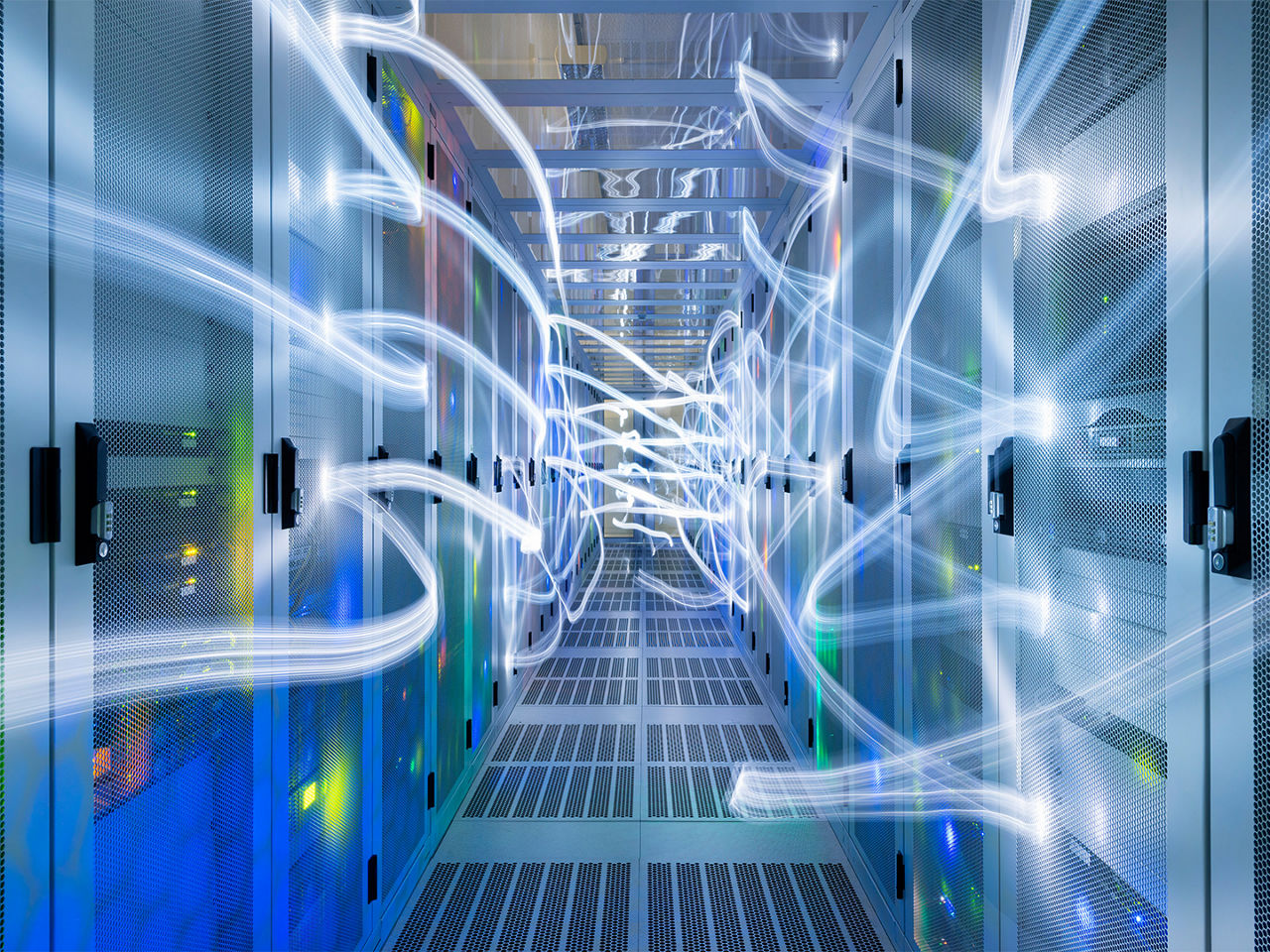 未来的なデータセンターの通路。高速データ転送と接続性を象徴する、ブルーとピンクの光の線に照らされている。