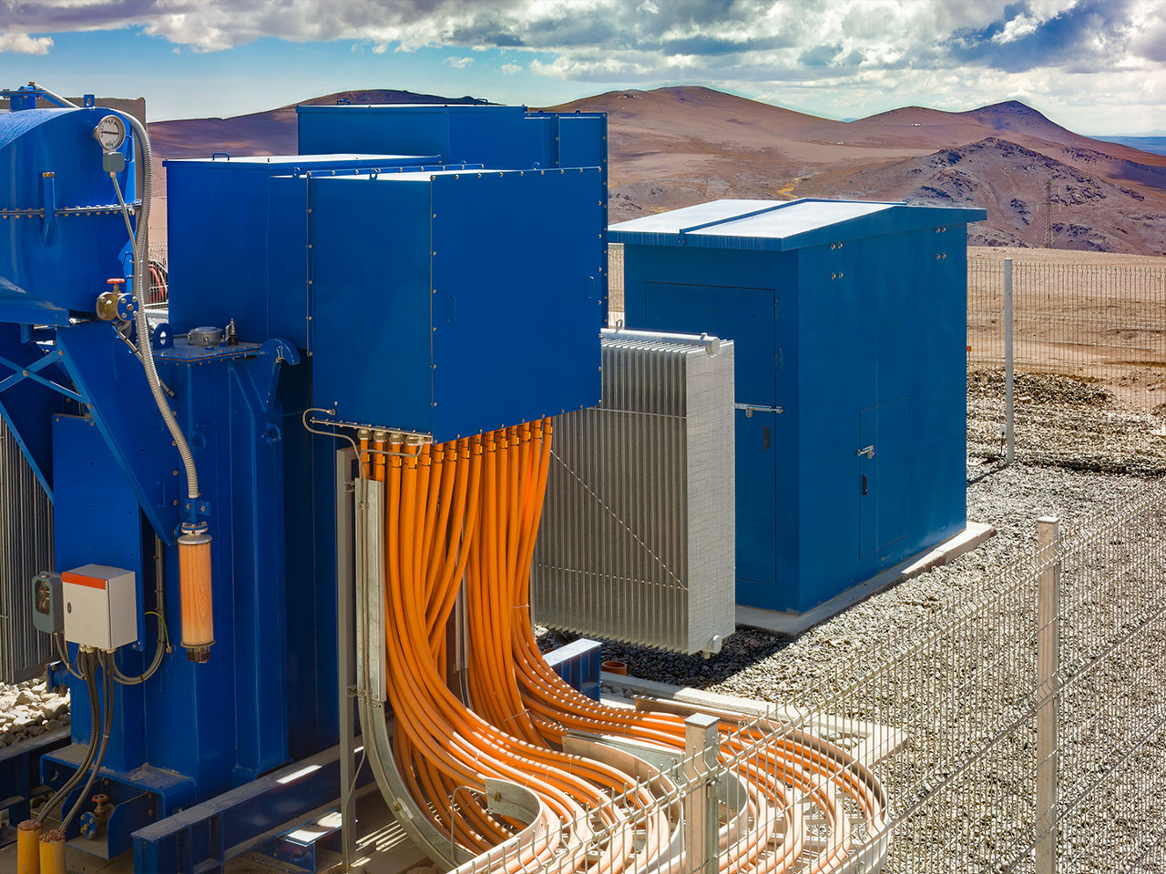 Orange industrial cables connect to blue equipment in a fenced desert facility built for harsh environmental conditions.