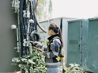 A field technician uses handheld test equipment to inspect telecommunications cables and network hardware.