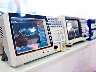 Digital spectrum analyzer and RF test equipment display signal measurements in an electronics laboratory.