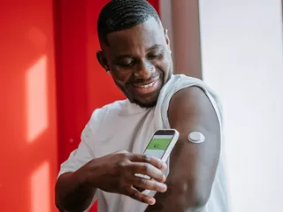 A man uses a smartphone to monitor data from a compact medical wearable sensor on his upper arm.
