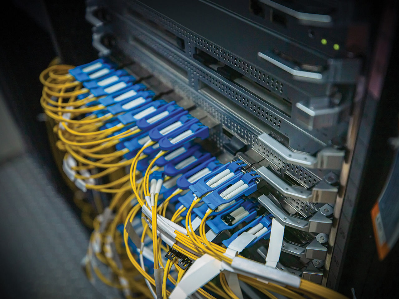 Computer network server cabinet with yellow fiber optic cables connected to blue transceivers.