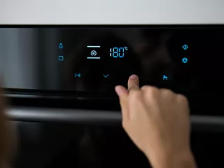 A person presses a button on the touchscreen control panel of a modern electric oven.