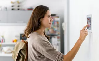 A person uses a wall-mounted touchscreen to control connected home appliances in a modern kitchen.