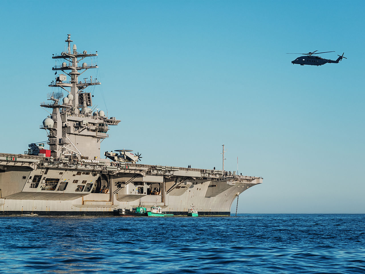 A US Navy aircraft carrier with a helicopter flying in the background.