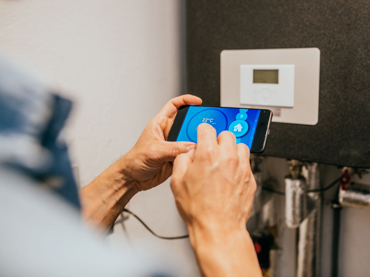 Person adjusting smart thermostat via smartphone interface. 