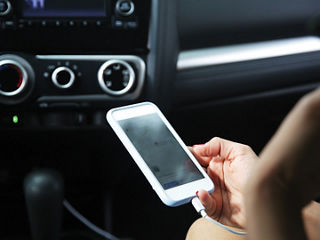 Person in an automobile holding a mobile phone that is plugged into a charger.
