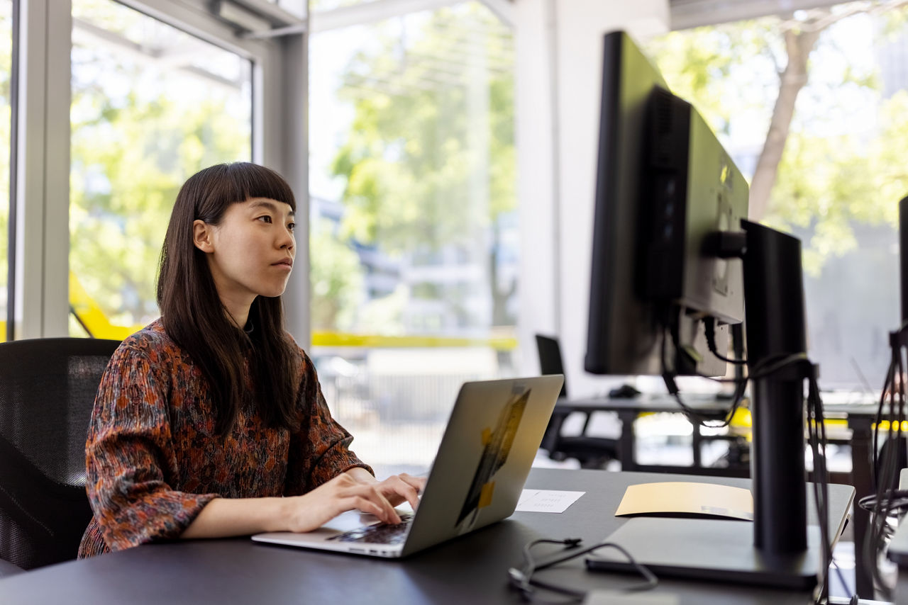 Young woman using laptop and looking at desktop monitor. Businesswoman working at her office desk.