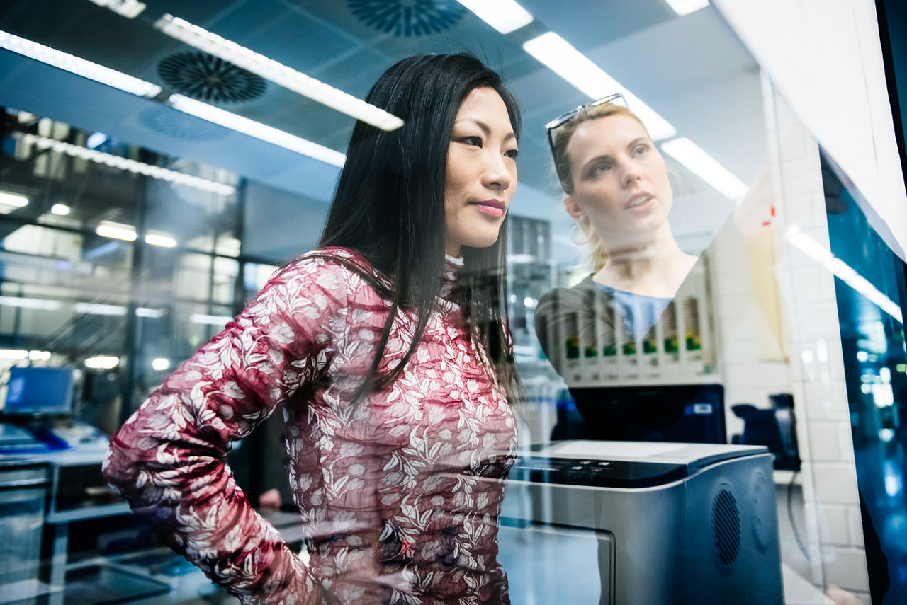 Two female engineers discussing a project in an industrial office while looking at documents pinned on a glass wall