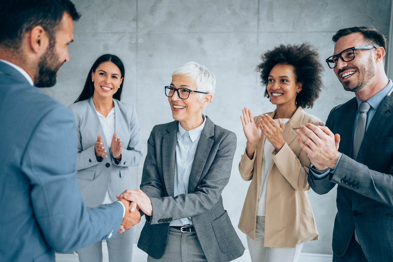 Business people shaking hands in the office. Business persons handshaking during a meeting in modern office. Group of cheerful business persons shaking hands and applauding.