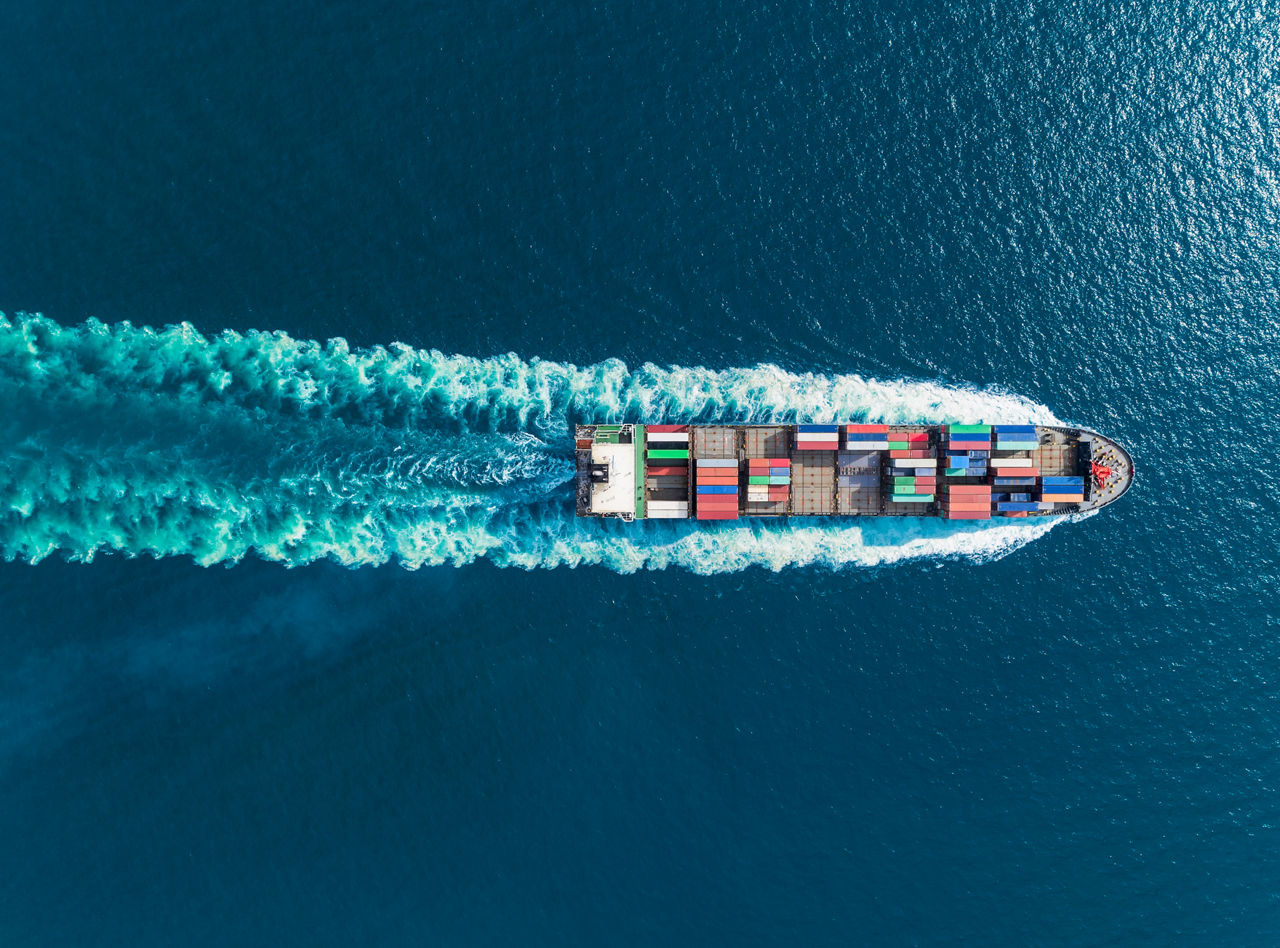 Aerial top view container ship full speed with beautiful wave pattern for logistics, import export, shipping or transportation.