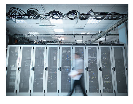 高性能データセンター内のサーバーラックの前を、モーションブラーがかかった技術者が歩いている。